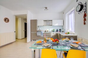 A modern kitchen with stainless steel appliances, a dining area with a glass table, and a decorative wall clock. - Asia Apartment: 2BR in Laveno Center (Laveno Mombello)