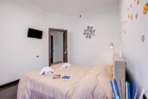 Une chambre d’hôtel comprenant un lit, un téléviseur à écran plat, un miroir, une horloge murale et une table de chevet avec une lampe.