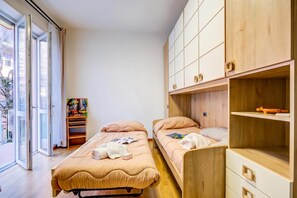 A room with two beds, a wooden cabinet, and a window with a view of the outside. - Asia Apartment: 2BR in Laveno Center (Laveno Mombello)