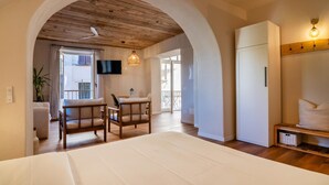Un dormitorio con una cama grande, techo de madera, televisor, zona de comedor con sillas y un balcón.