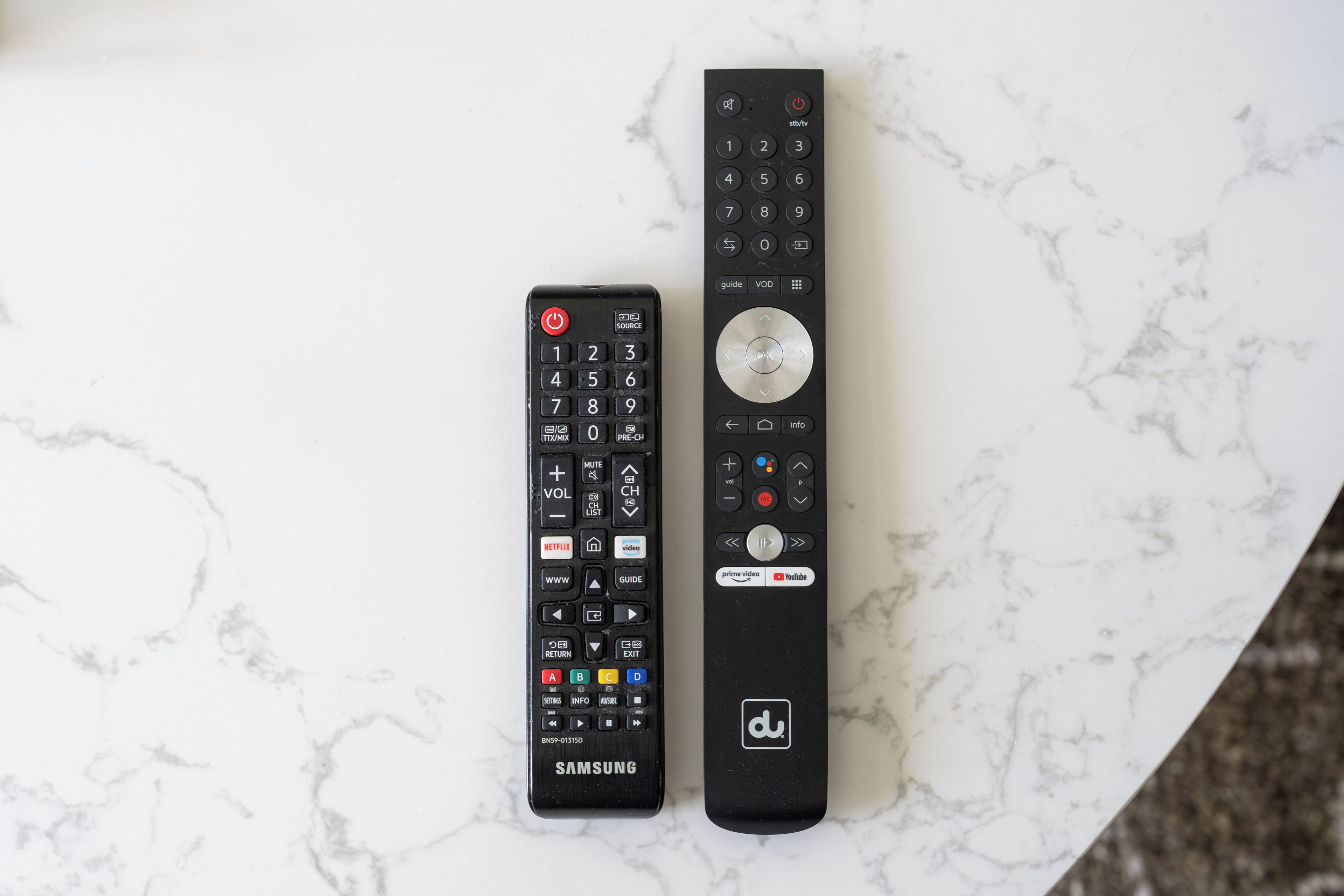 Two remote controls on a marble surface.