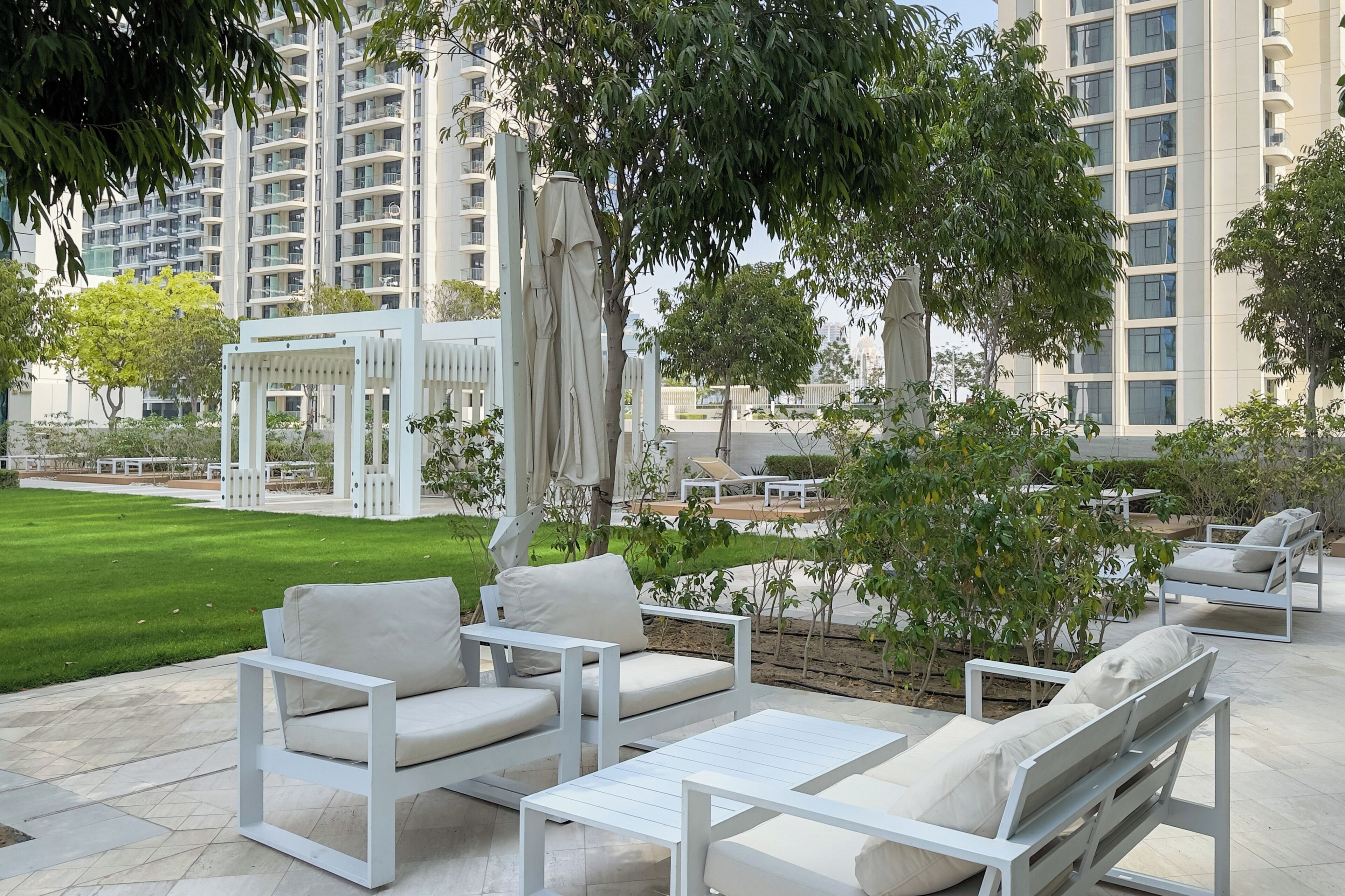 Een terras met wit meubilair, een pergola en uitzicht op hoge gebouwen.