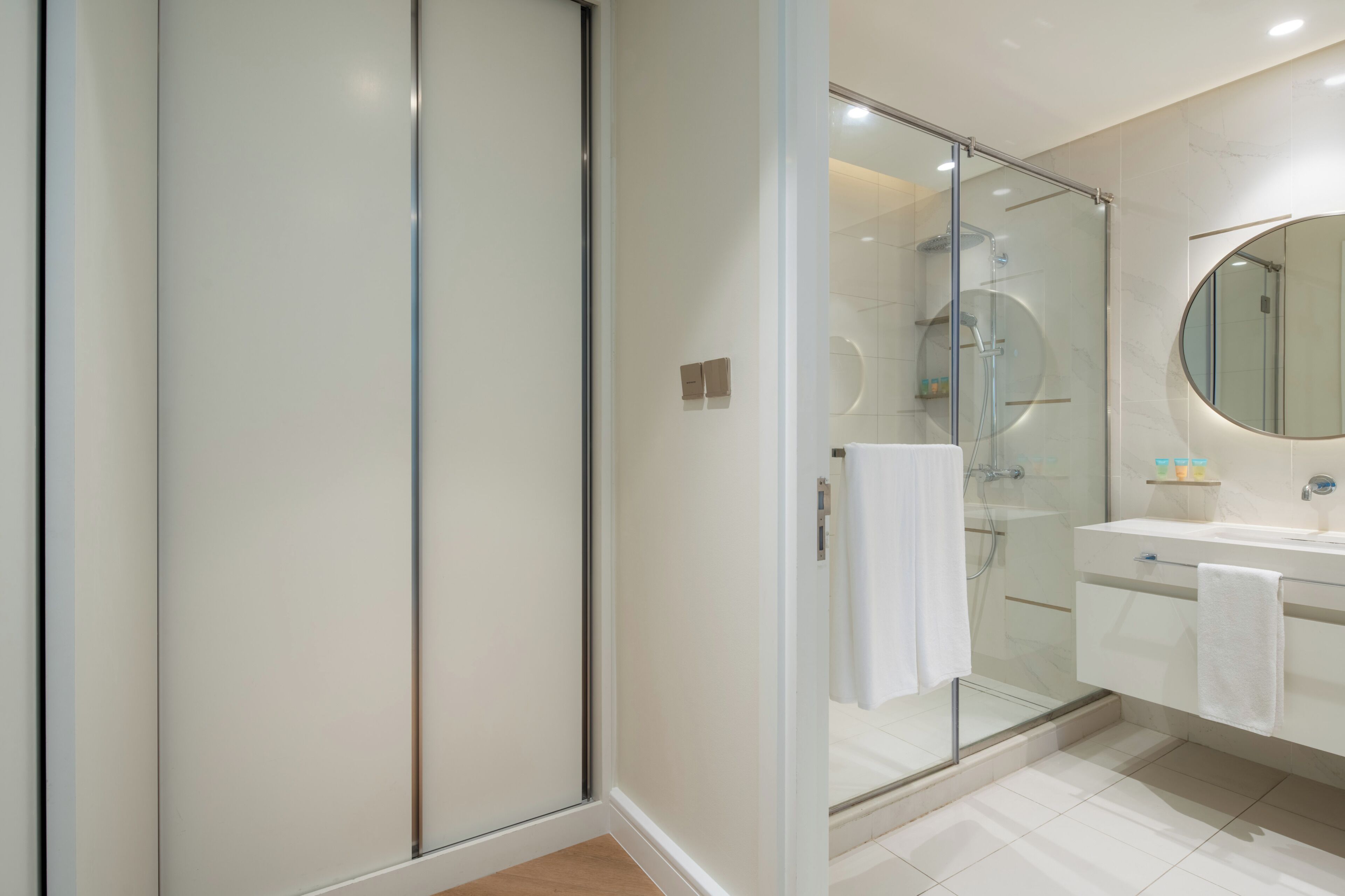 Une salle de bain moderne avec une douche à parois de verre, un miroir rond et un lavabo blanc.