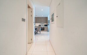 A hallway leading to a kitchen with a dining area, white walls, and a tiled floor. - Beachfront Marina Skyline Views (Dubai)