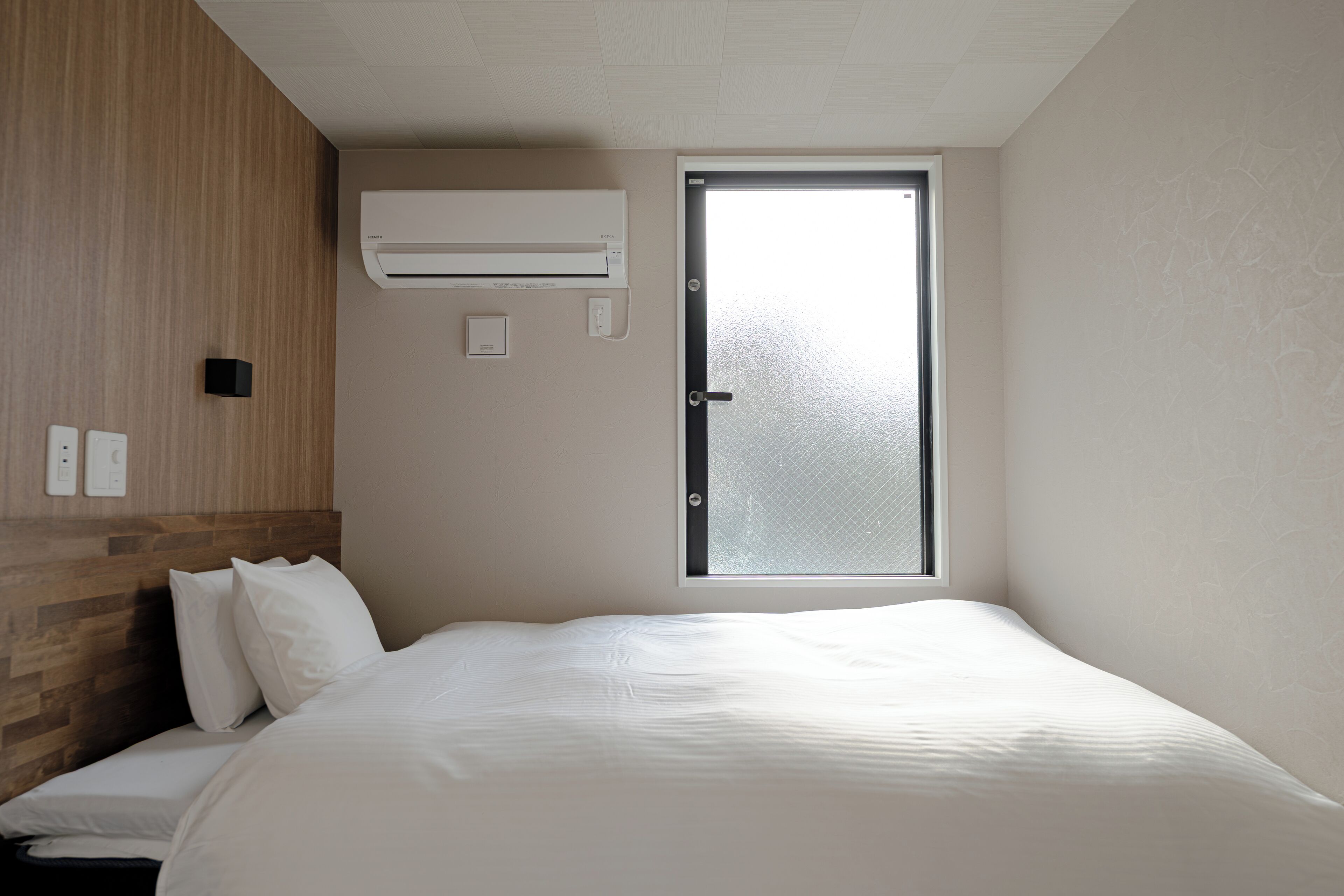 A hotel room with a bed, a window, an air conditioning unit, and a wooden headboard.