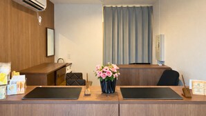 A hotel reception desk with two black tablet computers, a vase with pink flowers, a wooden desk, a chair, and a television on a stand. - Hotel Cradle Cabin TANASHI (Nishitokyo)