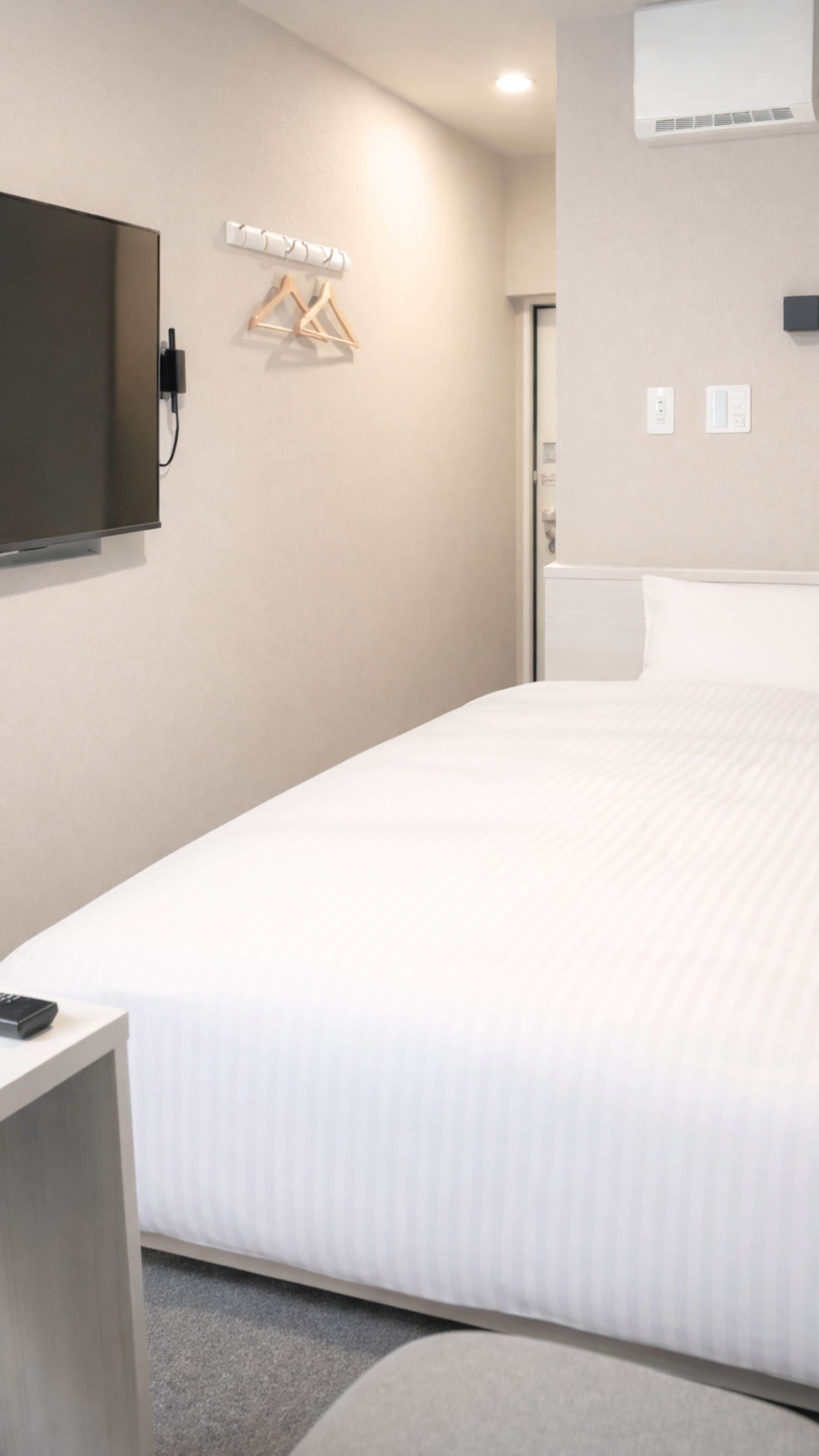 A hotel room with a large bed, a flat-screen TV mounted on the wall, a bedside table, and a wall-mounted air conditioning unit.