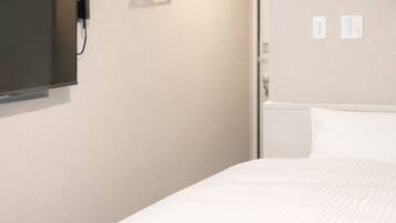 A hotel room with a large bed, a flat-screen TV mounted on the wall, a bedside table, and a wall-mounted air conditioning unit.