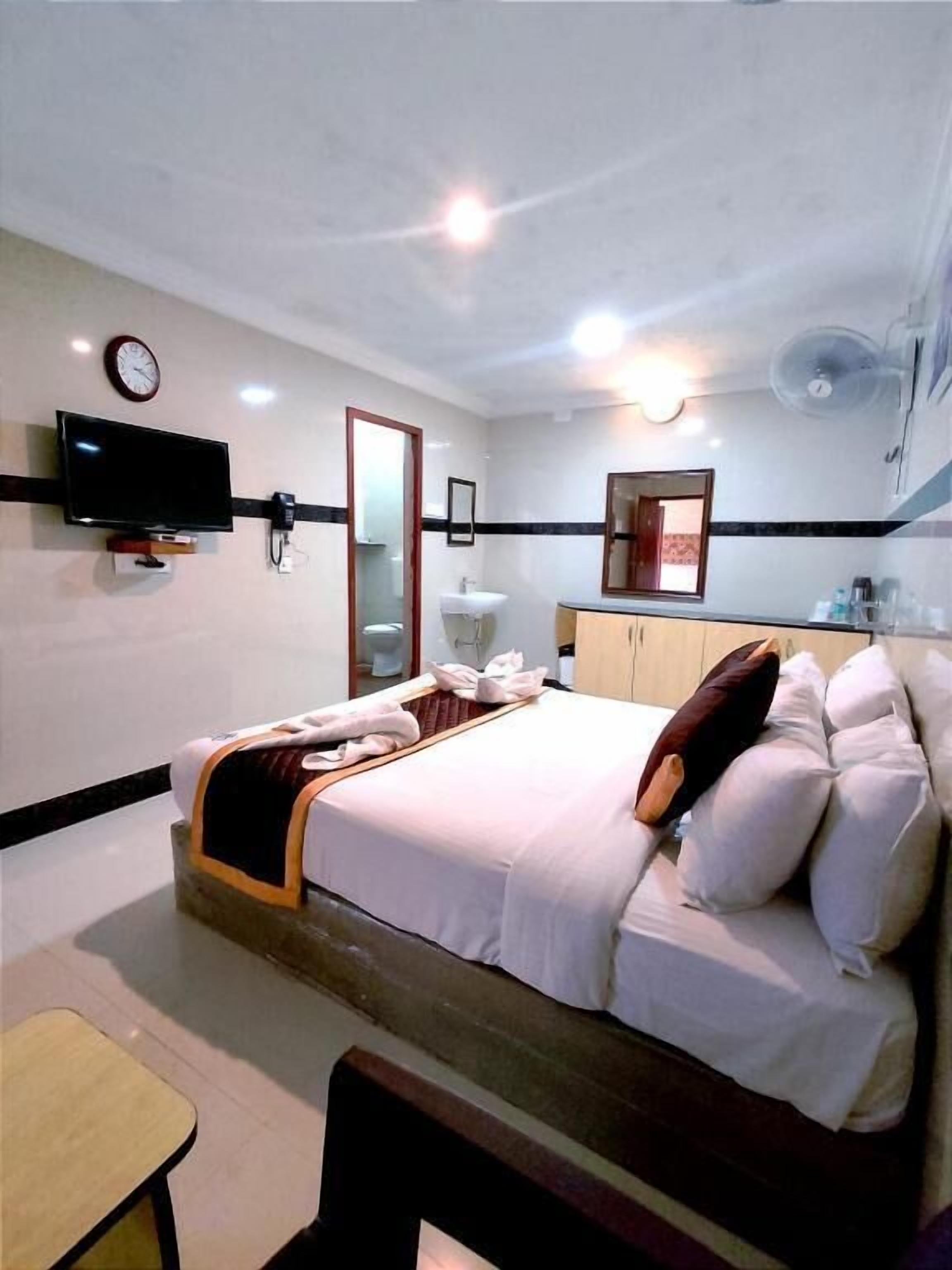 A hotel room with a bed, a TV mounted on the wall, a sink, and a mirror.