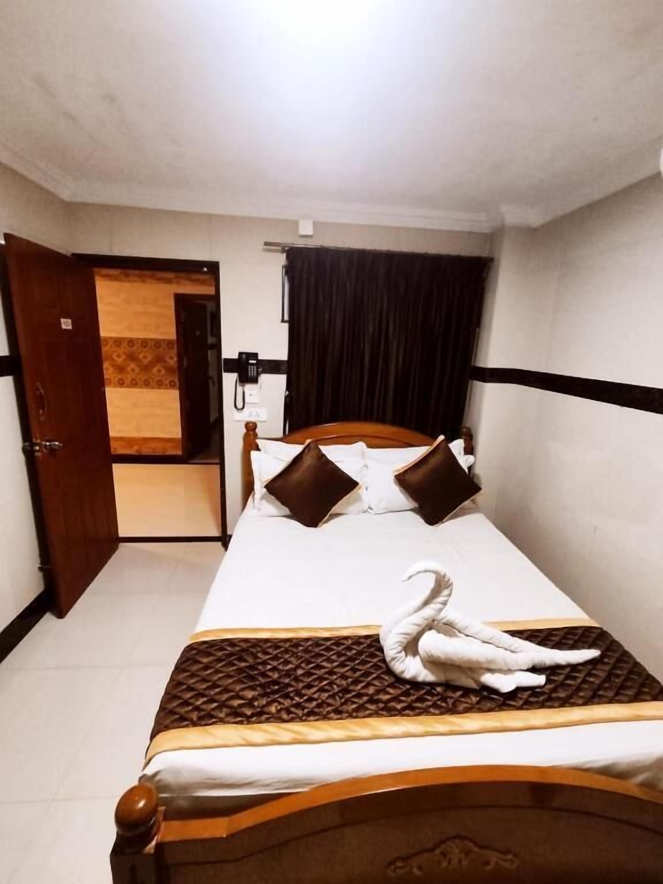 A hotel room with a bed, a wooden headboard, a telephone, and a curtain.