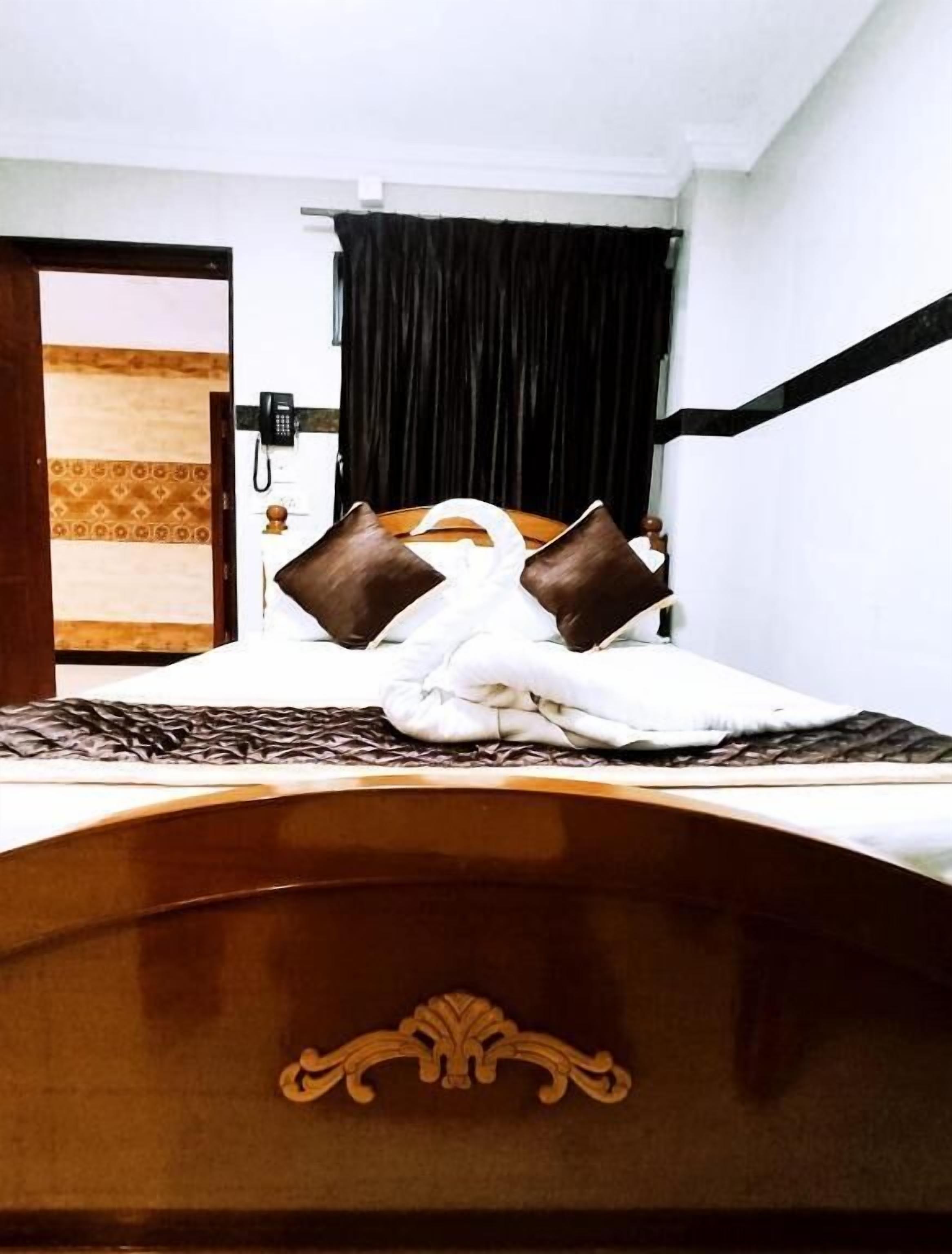 A hotel room with a wooden bed frame, a white bedspread, and two brown pillows.