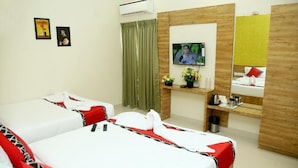 Quarto de hotel com duas camas, televisão, espelho, prateleira pequena com artigos de higiene pessoal e cortina verde.