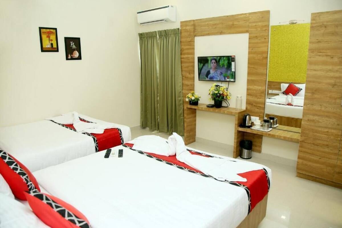 A hotel room with two beds, a TV, a mirror, a small shelf with toiletries, and a green curtain.