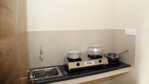 Cozinha compacta com fogão a gás, duas panelas e uma frigideira em bancada preta.