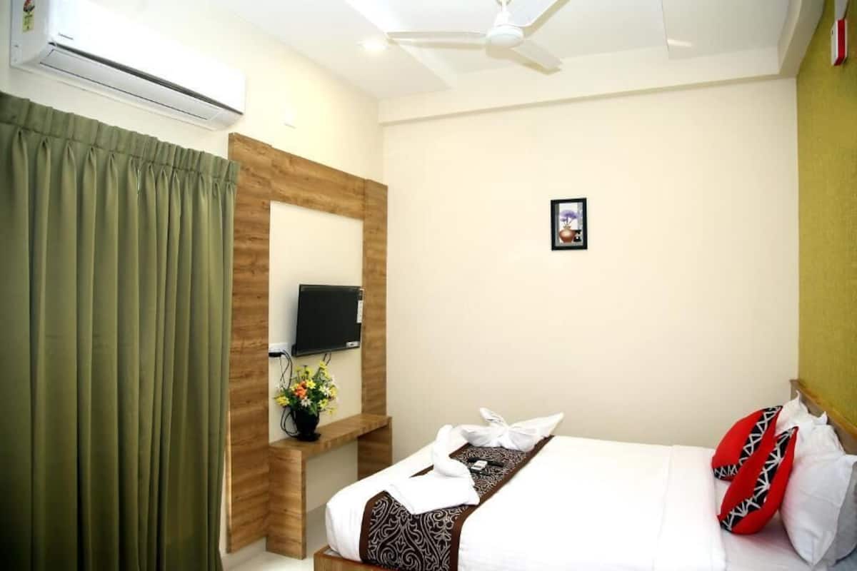 A hotel room with a bed, a TV, a wooden headboard, a small table with a vase of flowers, and a picture on the wall.