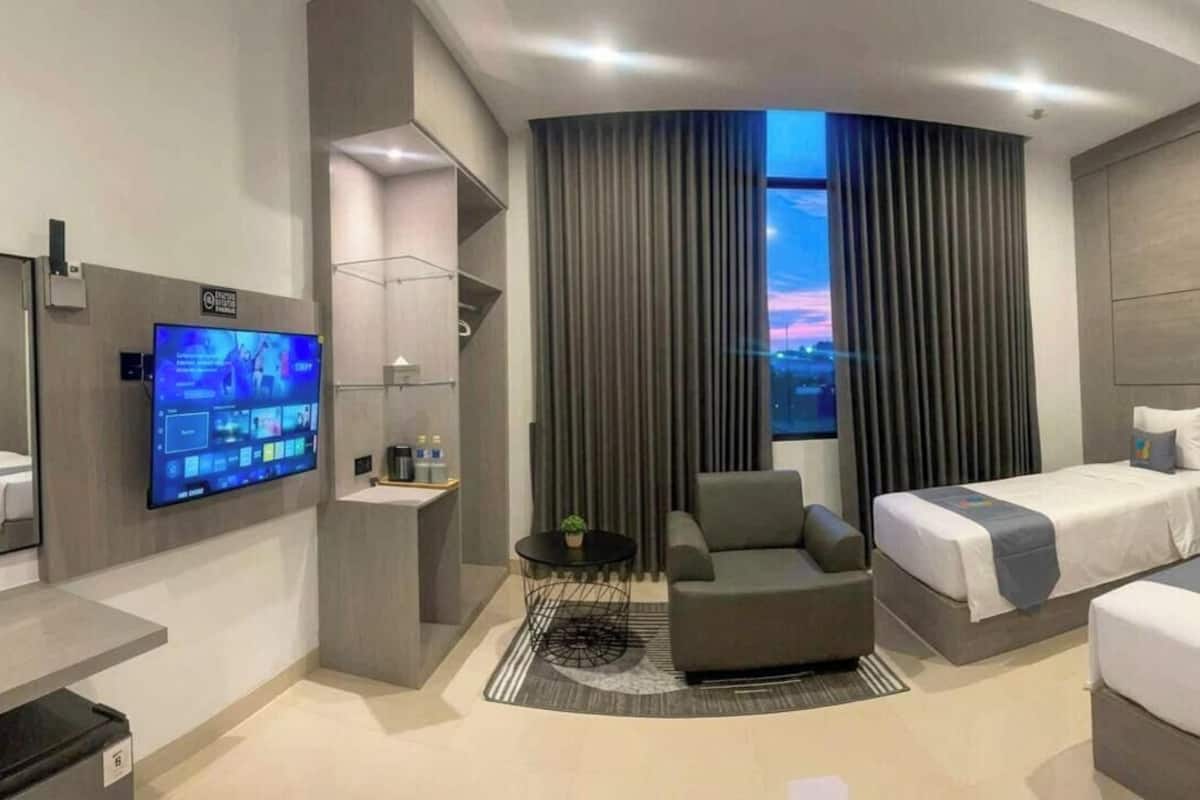 Una habitación de hotel moderna con un ventanal curvo, un televisor de pantalla plana, un sofá, una cama y una pequeña mesa.