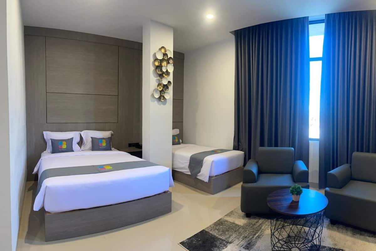 Una habitación de hotel con una cama grande, dos camas más pequeñas, un sofá, una mesa de centro y un adorno de pared.