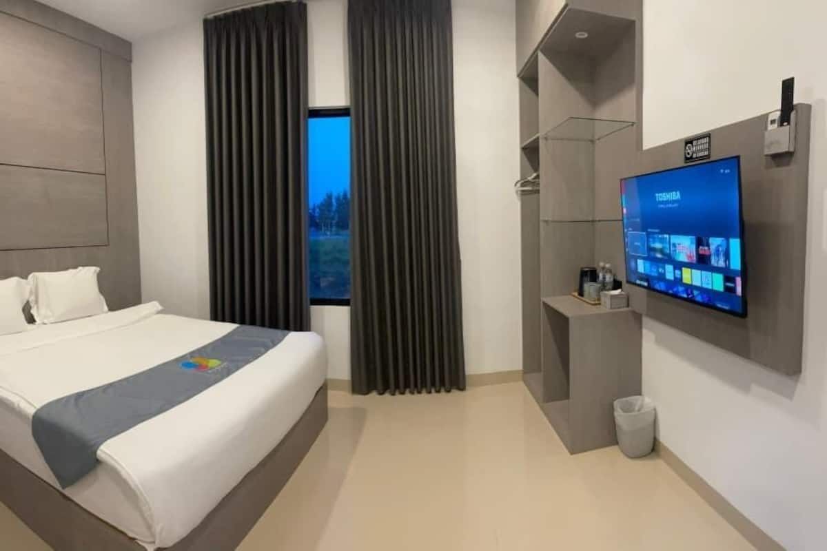 Una habitación de hotel moderna con una cama grande, un televisor montado en la pared y vistas al exterior a través de la ventana.
