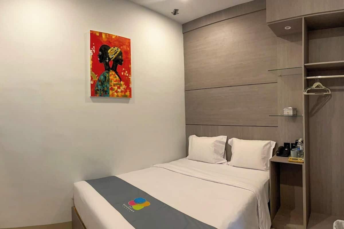Una habitación de hotel con una cama, televisión montada en la pared, armario y un cuadro.
