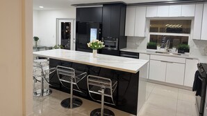 A modern kitchen with a central island, bar stools, a black refrigerator, and white cabinets.