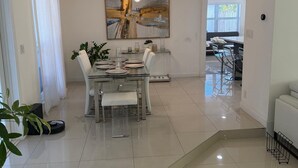 A modern dining area with a glass table, white chairs, and a large abstract painting on the wall.