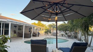 A covered outdoor area with a pool, lounge chairs, and a patio with a pergola.