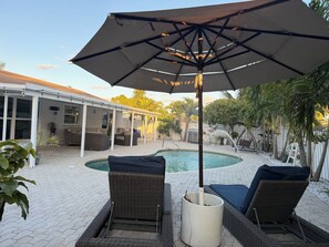A covered outdoor area with a pool, lounge chairs, and a patio with a pergola.