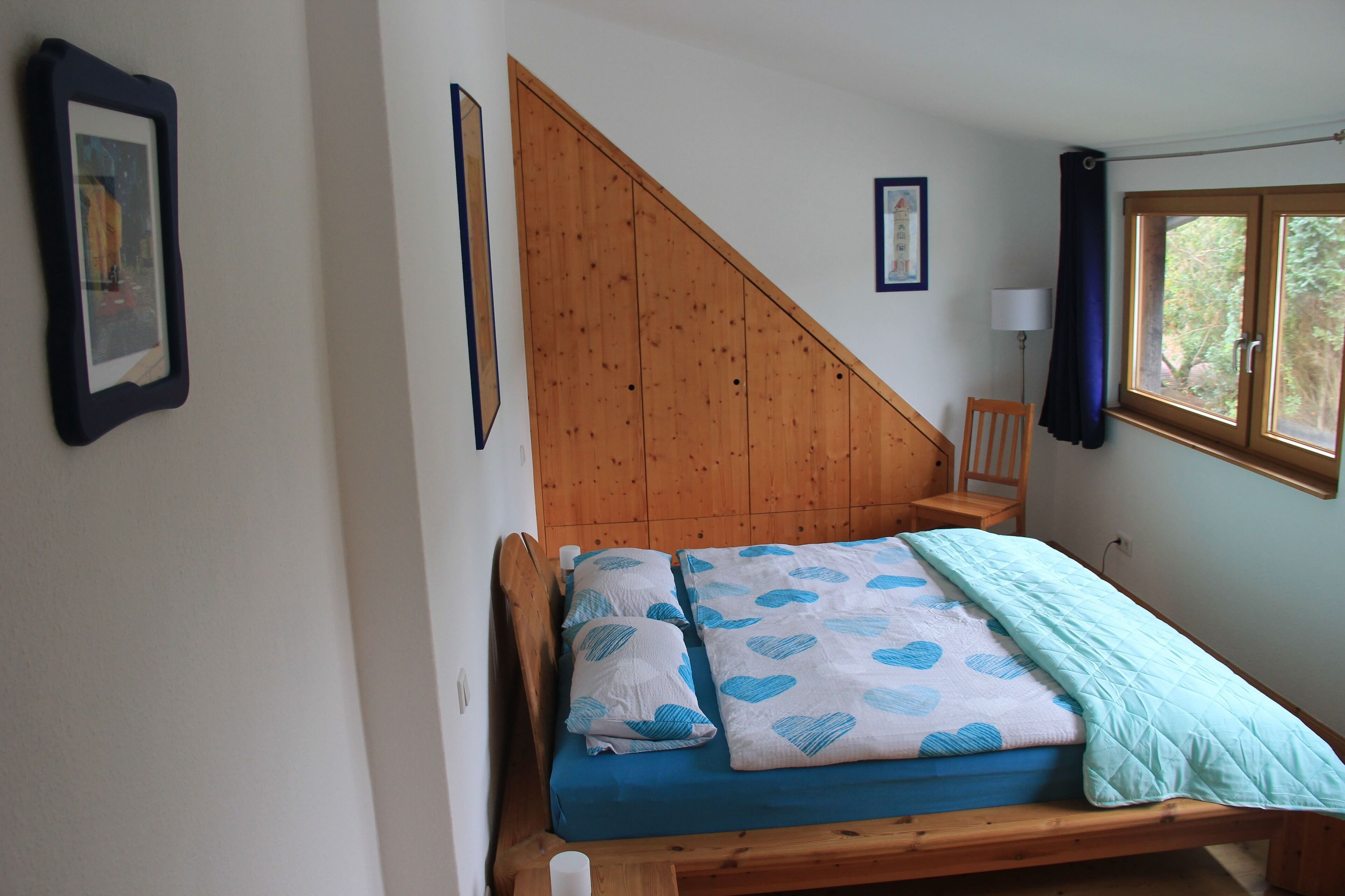 Une chambre à coucher avec un lit en bois, une couvre-lit bleue et blanche à motifs de cœurs et une tête de lit en bois.