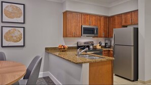 Eine moderne Küche mit Holzschränken, einem Edelstahlkühlschrank, einer Mikrowelle und einer Arbeitsplatte aus Granit.