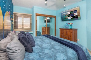 Une chambre à coucher avec un lit, un téléviseur fixé au mur, une armoire en bois et une fenêtre avec des stores.