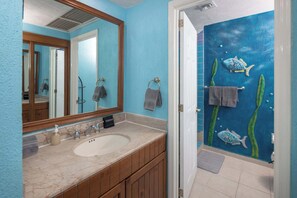 Une salle de bain avec un lavabo en marbre, des meubles en bois, un miroir et une fresque murale représentant des poissons et des algues.