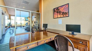 A hotel room with a wooden desk, two monitors, a wicker chair, and a glass wall leading to a gym area. - Seaside Serenity at Sonoran Spa N704 (Puerto Peñasco)