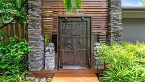 Una puerta de madera con un portón de metal, flanqueada por pilares de piedra y rodeada de abundante vegetación.
