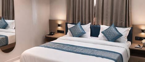 A modern hotel room with a large bed, a ceiling fan, an air conditioning unit, and a bedside table with a lamp.