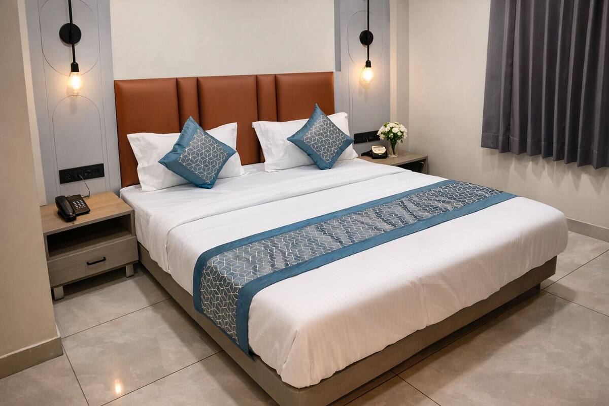 A neatly made bed with a patterned bedspread, a wooden nightstand with a phone, and a wall-mounted light fixture.