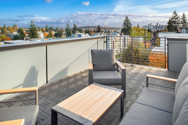 A rooftop terrace with a wooden table and grey seating, overlooking a cityscape with autumn foliage and buildings. - Lake View Townhouse (Seattle)