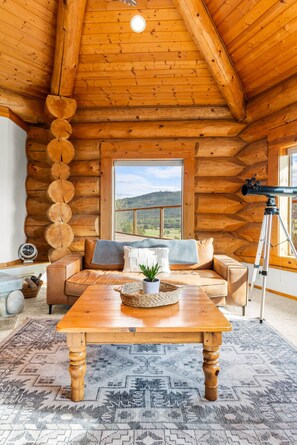 A log cabin interior with a wooden ceiling, a sofa, a table, and a telescope. - Log Cabin Retreat on Peaceful 5 Acres with Epic Views (Bell Hill)