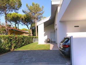 A modern building with a paved driveway, a parked car, and a well-maintained lawn. - Holiday apartment with air conditioning, terrace and garden (Bibione)