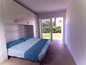 Un dormitorio con cama, armarios empotrados y puerta corrediza de cristal que da a un jardín.