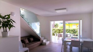 Ein modernes Wohnzimmer mit Treppe, Essbereich und einer großen Glasschiebetür, die auf eine Terrasse im Freien führt.