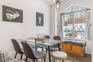 Un coin repas avec une table en verre, des chaises à revêtement gris, un panier en osier et un banc en bois agrémenté d’un plaid en fourrure.