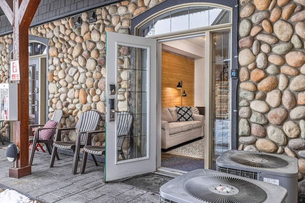 Une façade en pierre avec une porte en verre donnant sur un espace de vie comprenant un canapé et une table basse.