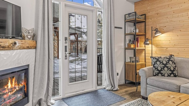 Ett mysigt vardagsrum med en öppen spis, en väggpanel av trä, en soffa och en bokhylla.