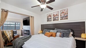 Una camera da letto con un letto grande, un ventilatore a soffitto, un camino e opere d'arte a tema montano sulla parete.
