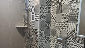 Un baño con pared de azulejos estampados, un inodoro, un lavabo y una zona de ducha.