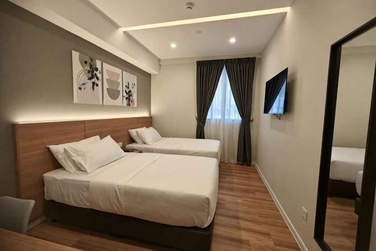 A hotel room with two beds, a flat-screen TV, a large mirror, and a window with curtains.