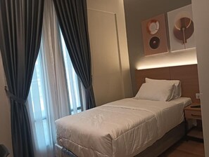 Ein Hotelzimmer mit Bett, Nachttisch, Schreibtisch und einem Fenster mit Vorhängen.