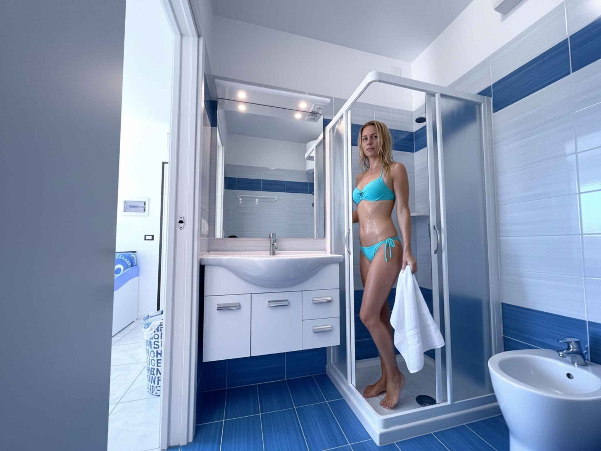 Ein modernes Badezimmer mit einer Duschkabine aus Glas, einem weißen Waschbecken und blautonierten Wandfliesen.