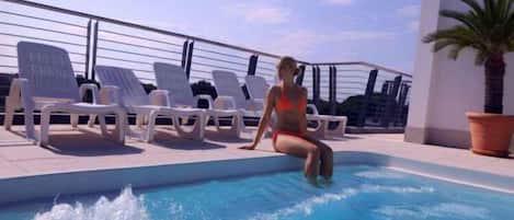 A pool area with lounge chairs and a person sitting by the pool.
