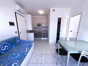 Una habitación pequeña con cama, una mesita y un kitchenette.